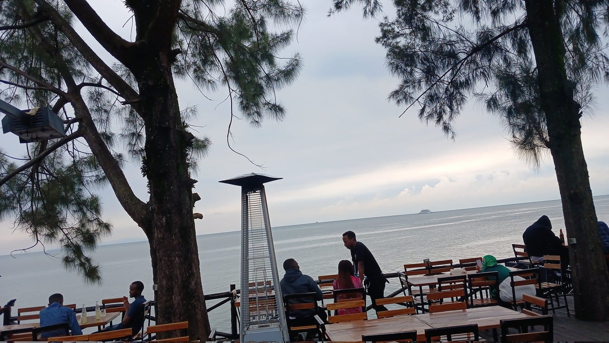 Guests on the deck under the pine trees, looking out over Lake Kivu