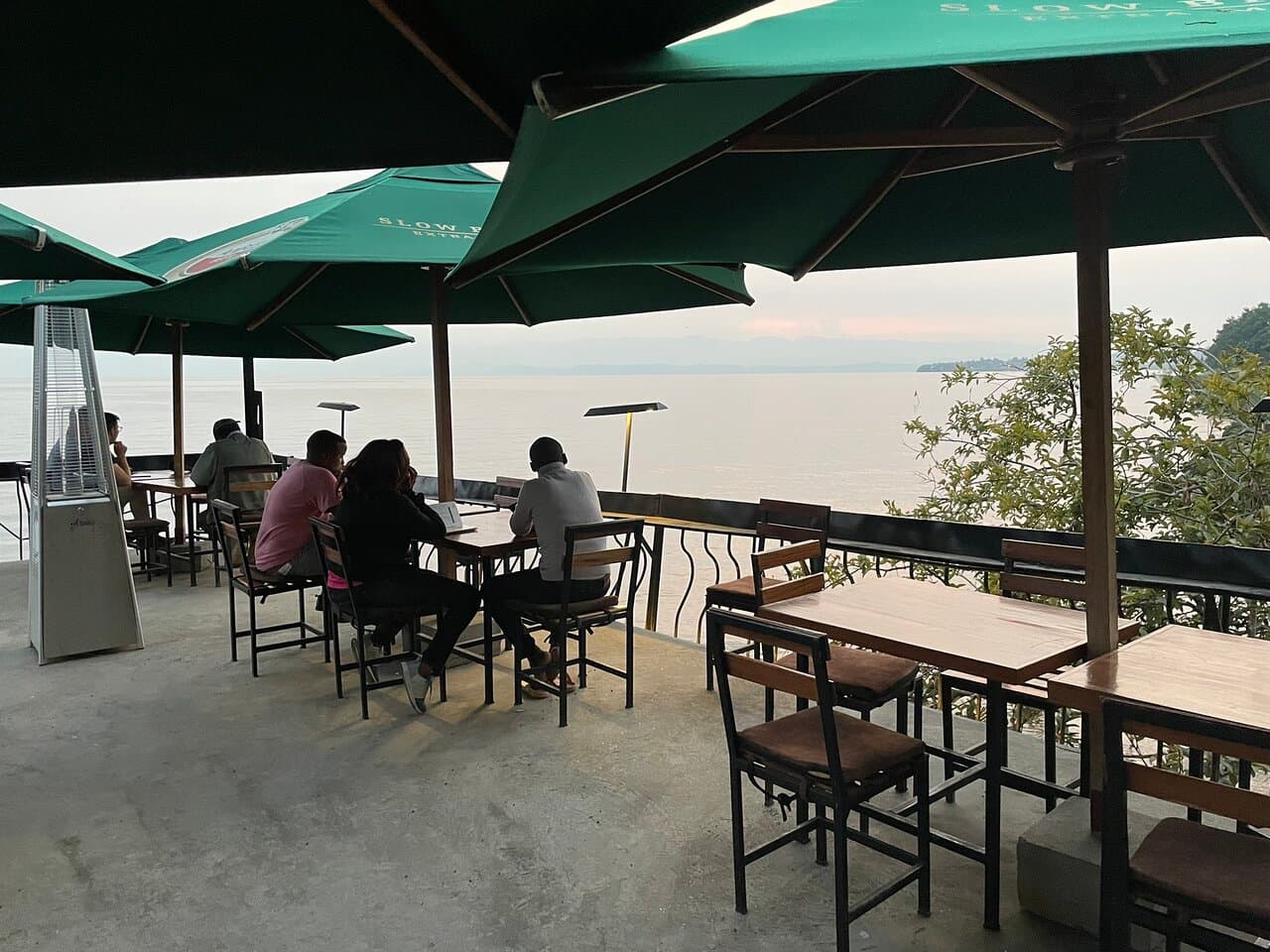 Guests eating under green umbrellas on the terrace above the lake